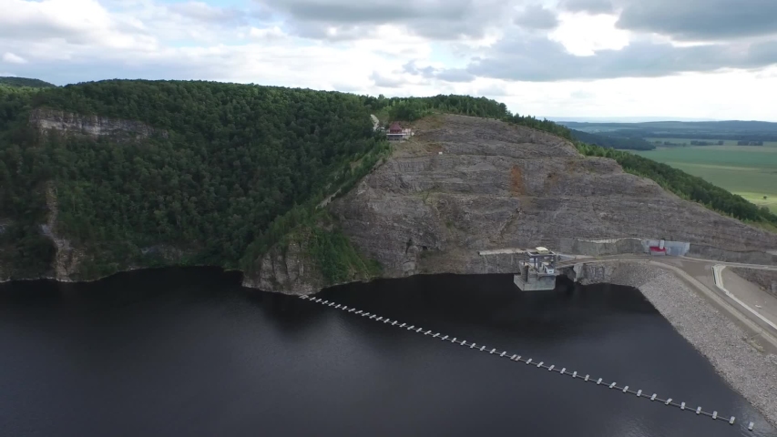 rocky shore surrounded by forest, small arbor and dam below, video from a drone