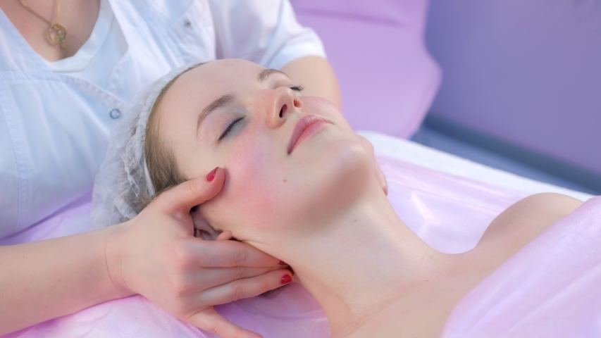 Cosmetologist massagist doctor making myoplastic neck massage to young woman, closeup portrait. Beauty spa procedure in cosmetology clinic. Doctor stroking and rubbing neck of young girl.