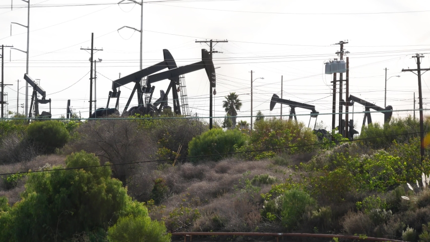 Industrial urban landscape. La Brea Inglewood in Los Angeles. Well pump jack operating behind the fence. Drilling rig extract crude oil. Oil mining machine with working piston. Oil and gas industry.