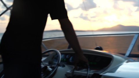 a man drives a motor boat, a yacht against the backdrop of the rising sun on the horizon, only hands and a helm are visible