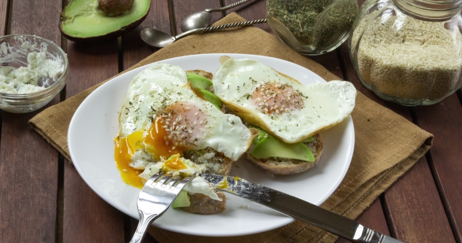 The process of preparing and eating Open avocado sandwiches made of slices of bread with ricotta cheese, avocado, fresh fried eggs and seeds. 4k, stop motion animation Royalty-Free Stock Footage #1052359990