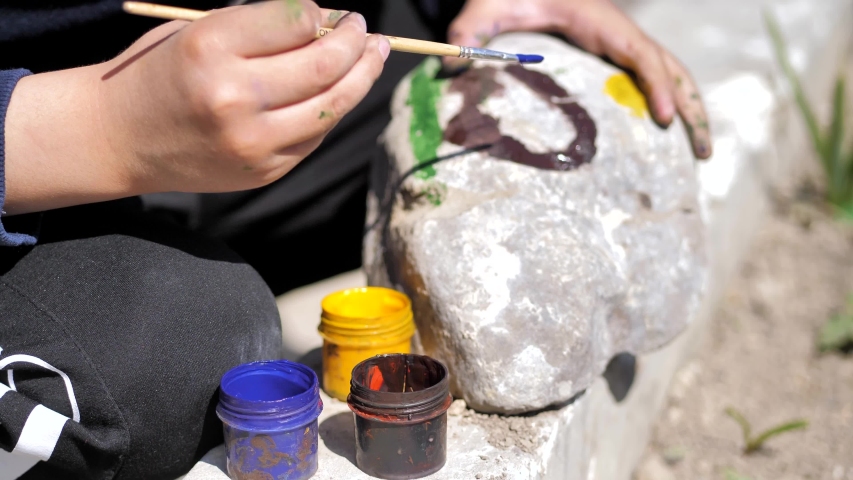The boy is sitting on his haunches and drawing on the stone. Drawn car on the stone