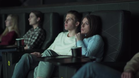 Young couple in a movie theater, watching a movie on a big screen and eating popcorn while watching a movie, a date, the effect of glowing light.