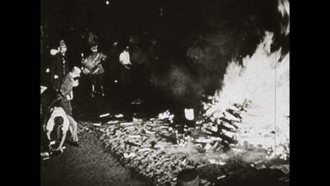 1960s: Man working in lab. Man adjusting controls. Close up of gauge moving. Waves moving on screen. Nazi soldiers marching. Close up of Adolf Hitler. Hitler saluting. Men throwing books on bonfire.