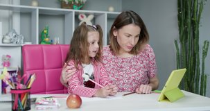 Mother and daughter doing homework online. Distance learning online education. Schoolgirl with digital tablet laptop notebook and doing school homework. Mom does homework with her daughter at home