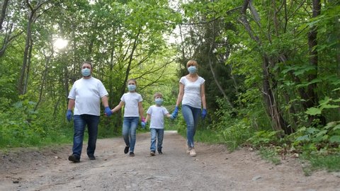 Family: father, mother, son and  daughter  walk in the Park in medical masks and white t-shirts and rubber gloves . slow motion . The concept of protection FROM covid-19 coronavirus infections.