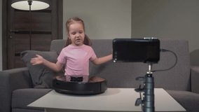 A little Caucasian girl shows the details of a vacuum cleaner robot to her subscribers online. Vacuum Cleaner Concept.