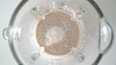 An electric blender, a mixer with a glass bowl, in which smoothies are prepared, porridge for whipping, pour protein powder with a measuring spoon in your hand. Top view.