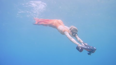 Beautiful young girl swimming underwater with mask and seabob enjoying nice refreshing water, wearing long red dress, summer vacation and travel concept