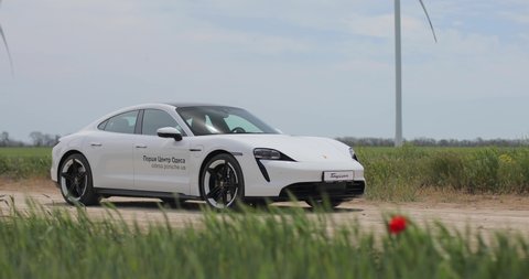 Odesa, Ukraine - May 11, 2020: Porsche Taycan Turbo In a field near wind-driven electric generators. Test drive Porsche Dealership Odesa Porsche Center.