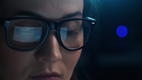 Close up of tired woman working at night on laptop, girl in eye glasses with reflections overworking busy, using computer in dark office