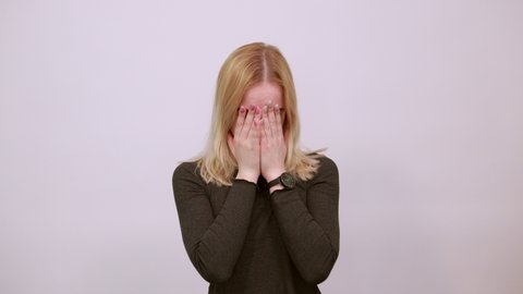 Young Blonde Woman In Black Sweater With Stylish Watch On White Background, A Scared Girl Holds Her Hands Clenched Into Fists Near Face. The Concept Of Fear, Uncertainty, Infirmity Of People
