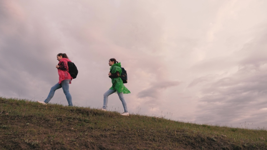 Free female travelers walk along the top of the hill. team work of travelers. The concept of adventure and travel. Healthy female tourists travel with backpacks in colorful raincoats, storm is coming | Shutterstock HD Video #1052390575