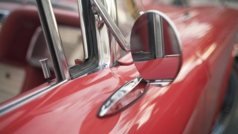 Details of red retro car on a blurred city background. Action. Close up of round rear view mirror of the old fashioned polished shiny red vehicle.