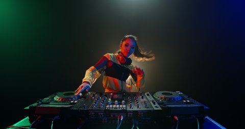 Cool female asian dj is working in a nightclub, standing at turntables, creating a dance music set - nightlife concept 4k footage