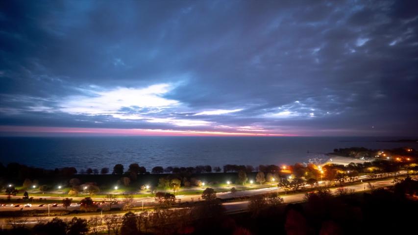 A beautiful pastel pink blue and purple sky sunrise timelapse over Lake Michigan as clouds roll overhead and traffic builds on Lake Shore Drive below.