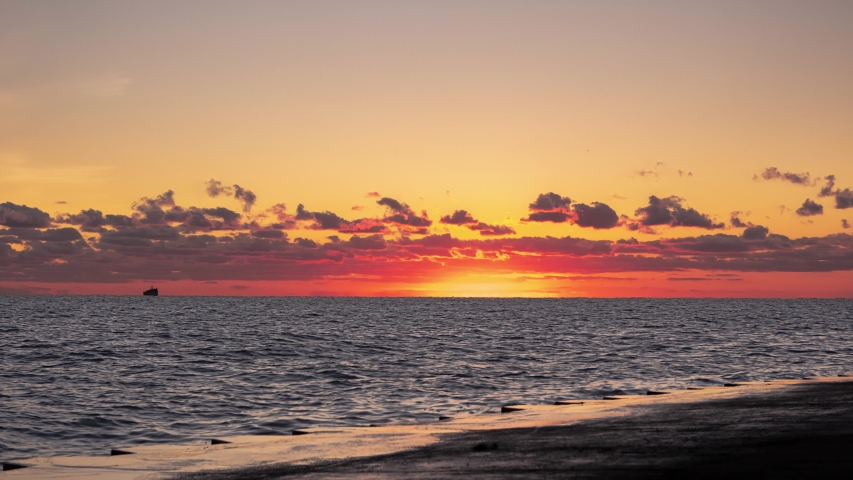 A beautiful zoom in panoramic orange and yellow sunrise timelapse over the water of Lake Michigan as the sun rises towards clouds just above the horizon as a flock of geese swim by.