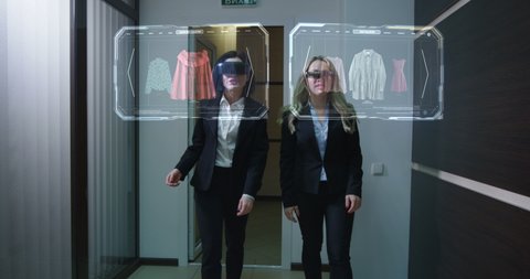 Medium long shot of two women walking through corridor while using holographic vr technology for online shopping