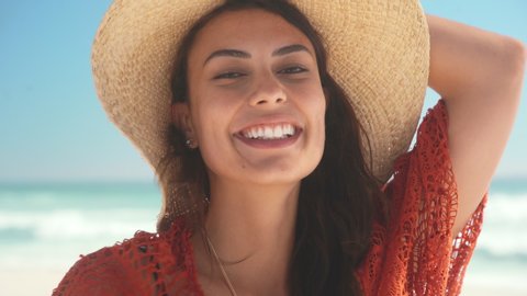 Portrait of young beauty woman with ocean in background. Beautiful fashion woman at the beach protecting from the sun with a big hat and copy space. Close up face of glamour girl looking at camera.
