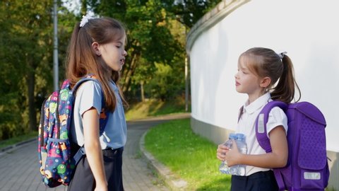 Little school children. Happy schoolgirl in uniform with Backpack Feeds a Squirrel in the Park on her way to School..