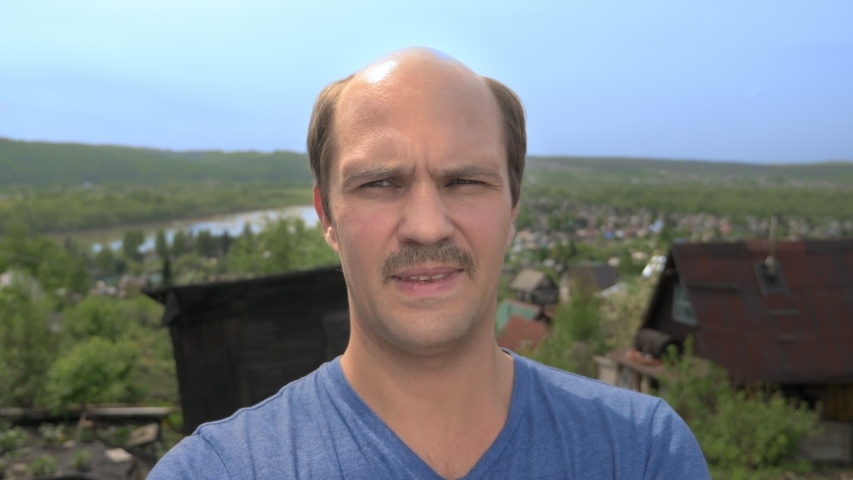 portrait, balding young man with mustache in the countryside looking at the camera, smiling