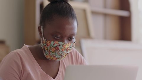 Close up of a young black female student working on her laptop while wearing a health mask. स्टॉक वीडियो