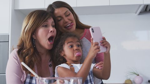 Multi-generation Hispanic female family taking selfie on mobile phone whilst making cake in kitchen together - shot in slow motion