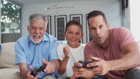 Multi-generation male Hispanic family sitting on sofa at home playing video game together - shot in slow motion