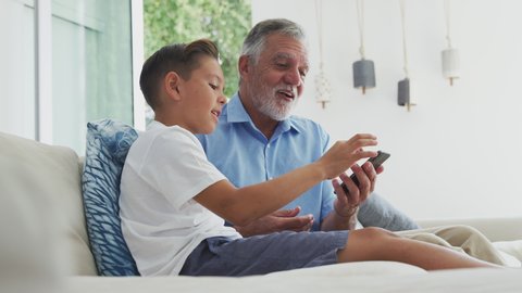 Hispanic grandson showing grandfather how to use mobile phone at home - shot in slow motion