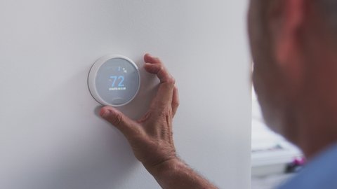 Senior Hispanic man adjusting digital central heating thermostat in home - shot in slow motion