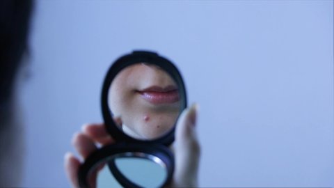 A woman looks at a pimple on her face in the mirror. Close up. Acne, redness, blemishes, blackheads. Skin care, cosmetology. Teen, hormones, oily skin. Panic, trouble, bad day.