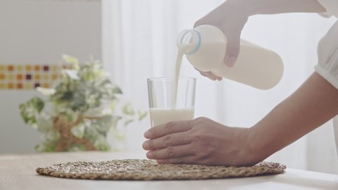  Hand of  Asian woman pouring milk into a glass in the kitchen at the home in the morning, Close- up hand young women. Health care concept