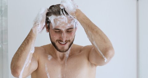 Young handsome bare man washing head with anti-dandruff shampoo lathering hair with foam. Attractive naked guy taking shower doing everyday fresh clean male haircare hygiene routine concept.