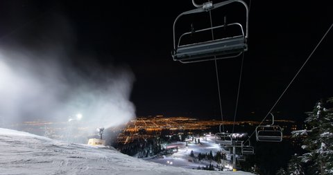 Panning time lapse shot of ski lift over snow blower on hill near illuminated city at night - Vancouver, Canada