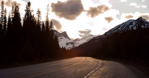 Lockdown time lapse shot of vehicles on road amidst trees and mountains against cloudy sky during sunset - Banff, Canada