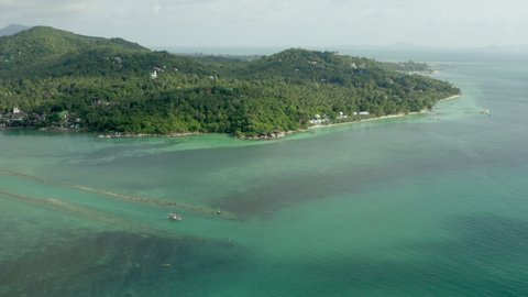 Aerial shot of boat in sea near green trees on island, drone flying forward towards forest on sunny day - Ko Pha Ngan, Thailand