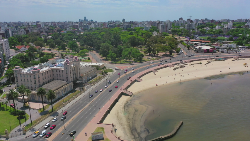 Aerial shot of vehicles on road by buildings and trees in city, drone flying forward over beach against sky on sunny day - Montevideo, Uruguay | Shutterstock HD Video #1052449621