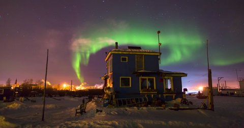 Lockdown time lapse shot of blue house on snow emitting smoke against polar lights at night - Northwest Territories, Canada