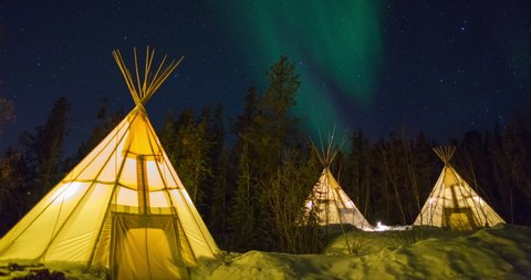 Lockdown time lapse shot of illuminated tents on snow by trees against sky at night - Northwest Territories, Canada