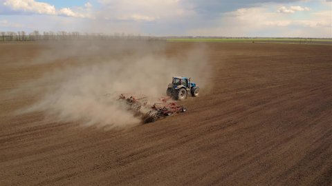 Aerial footage of modern blue tractor with red plough plowing or cultivating large field. Spring agronomic activity on agricultural land