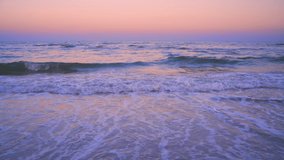 Dawn on the beach. Sea waves roll on the sandy beach. The pink sky is reflected in the water. Hua hin beach in Thailand.