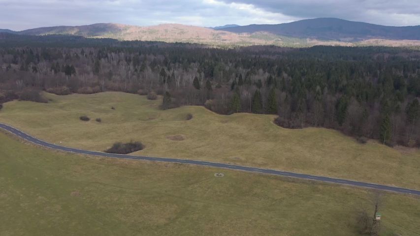 Aerial over forest and empty road. Mountains and clouds in the background. Late autumn season atmosphere.
