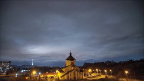 Beautiful time lapse: massive clouds floating night city sky. Orthodox church on foreground and lightened TV tower on background. 4K