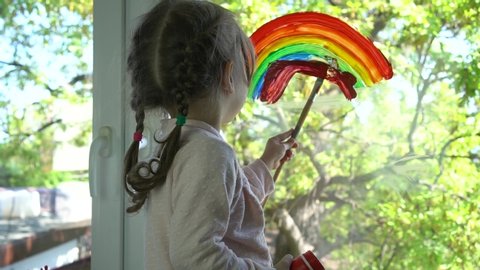 A child draws a rainbow on the glass of a balcony. Colourful rainbow pictures drawings on windowsspread hope during coronavirus pandemic. Covid-19 outbreak. Home lockdown
