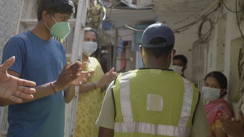 People men and women wearing protective face masks are outside their houses and clapping claps when health worker essential service provider doctor passing through a lane, Mumbai, India (May 2020)