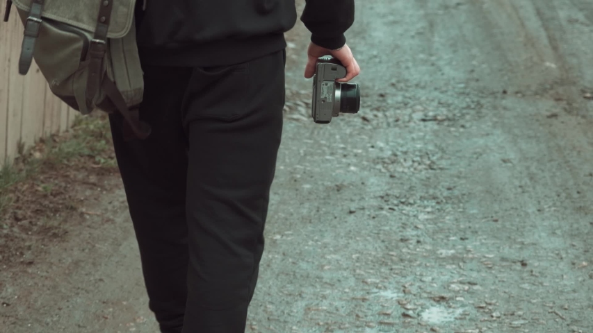A guy with a camera in his hand walks along a gravel road in slow motion