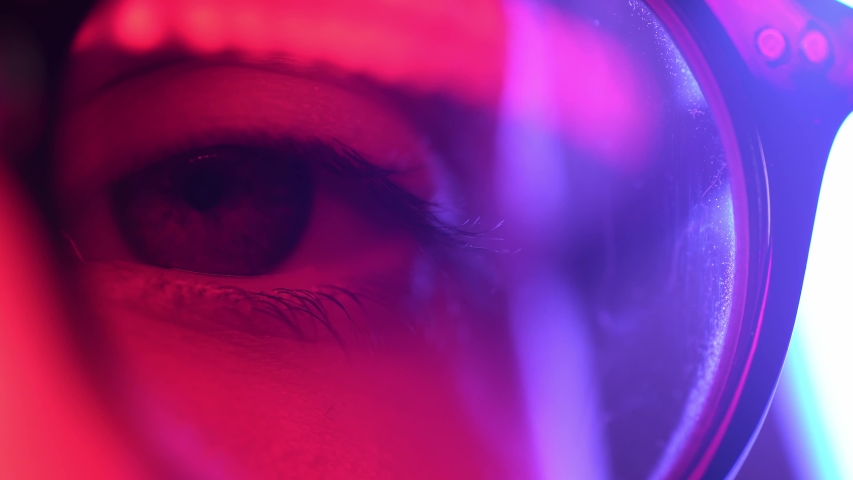 Close up macro woman blue eye in glases opening beautiful iris natural human in neon light. beauty healthy eyesight concept