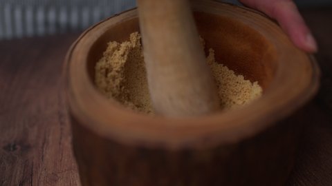 A woman hand crushing and grinding ingredients in a wooden mortar with a pestle into a fine powder.