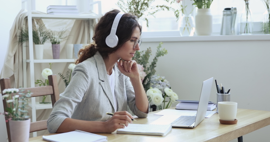 Female florist designer or wedding planner wearing headphones elearning, watching online webinar, making notes, conference video calling using laptop learning creative floristry decor training course. | Shutterstock HD Video #1052488891