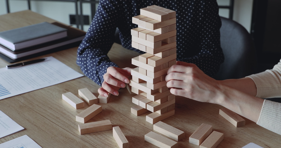 Two business women play build game in office. Female business partners hands take blocks out of wooden tower. Risky solutions in company building strategy plan, help in teamwork concept. Close up view Royalty-Free Stock Footage #1052489983